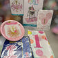 A 1st birthday party decoration kit containing a pink and gold '1st Birthday' plate, a party hat napkin, a balloon print, a high chair mat, and a blue napkin cover, all in retail packaging.