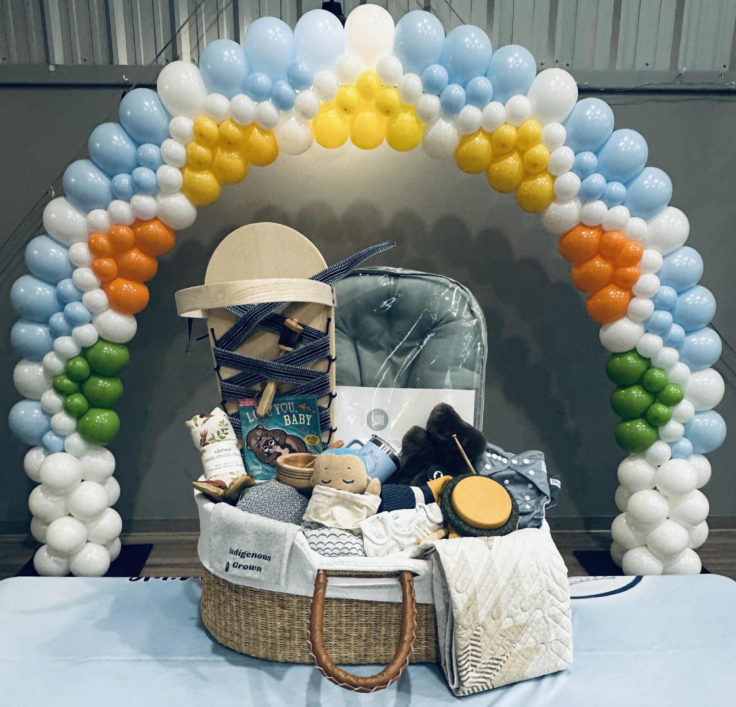 Baby gift basket with baby items under a colorful balloon arch