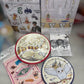 A Harry Potter themed party decoration kit displayed with its packaging and contents, including printed plates, napkins, and small accessories on a blurred gray surface.