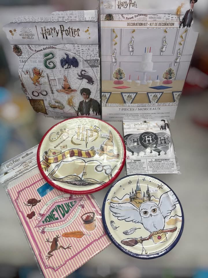A Harry Potter themed party decoration kit displayed with its packaging and contents, including printed plates, napkins, and small accessories on a blurred gray surface.